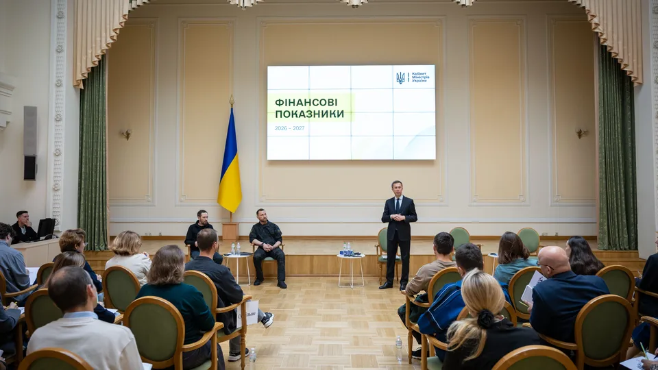 Загальний план зали: промовець перед екраном «Фінансові показники», слухачі та прапор України.